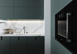 Keramik-Arbeitsplatte in heller Optik in einer cleanen Küche mit dunkelgrünen Fronten, einem integrierten Spülbecken mit schwarzer Armatur, einigen Tellern sowie einem Backofen auf Augenhöhe im Vordergrund