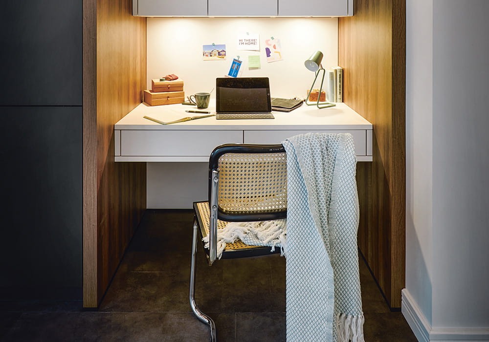 Blick auf eine Schreibtisch-Nische mit indirekter Beleuchtung, einem aufgeklappten Laptop sowie einem Stuhl mit einer darüber liegenden Decke davor